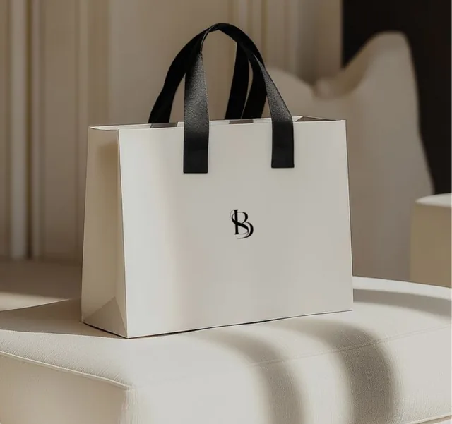 Ivory paper bag with black ribbon handles and a small black monogram