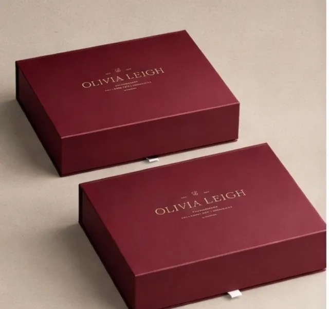 Two burgundy Olivia Leigh book-style rigid boxes with gold foil logos