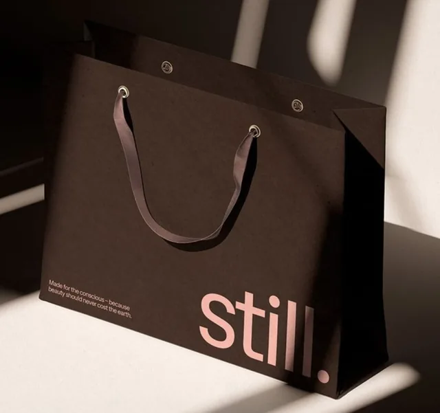 Dark brown paper bag with ribbon handles and pink lettering